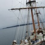 photograph of tall masted sailing ship on grey overcast day docked in Salish Sea with Whidbey Island in background